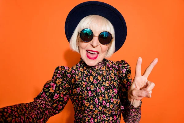 Retrato de sorrir alegre feliz mulher idosa positiva tirar selfie mostrando v-sinal isolado no fundo cor de laranja — Fotografia de Stock