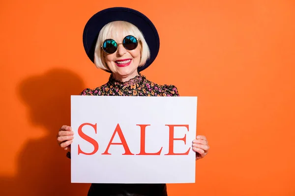 Porträt von glücklich lächelnd fröhlich positive alte Dame halten Verkauf Plakat tragen Sonnenbrille isoliert auf orangefarbenem Hintergrund — Stockfoto