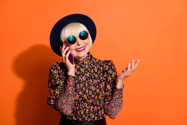 Foto de feliz alegre sonriente charla abuela funky en el teléfono use gafas de sol aisladas en el fondo de color naranja —  Fotos de Stock