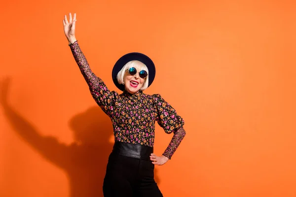 Foto de sorrindo louco alegre feliz bom humor avó levantar a mão usar óculos de sol isolados no fundo cor de laranja — Fotografia de Stock