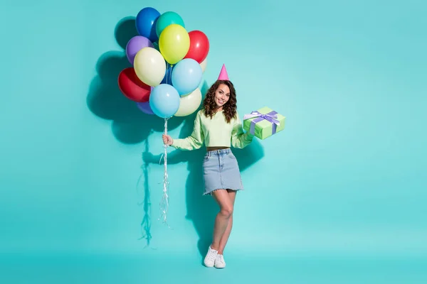 Foto de chica encantadora celebrar regalo manojo globos usar pantalones vaqueros suéter verde mini falda cono sombrero zapatillas aislado color azul fondo — Foto de Stock