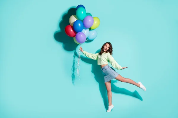 Foto de la señora bastante joven sostienen muchos globos que se divierten usar zapatillas de deporte pantalones vaqueros jersey verde falda corta aislado color azul fondo — Foto de Stock