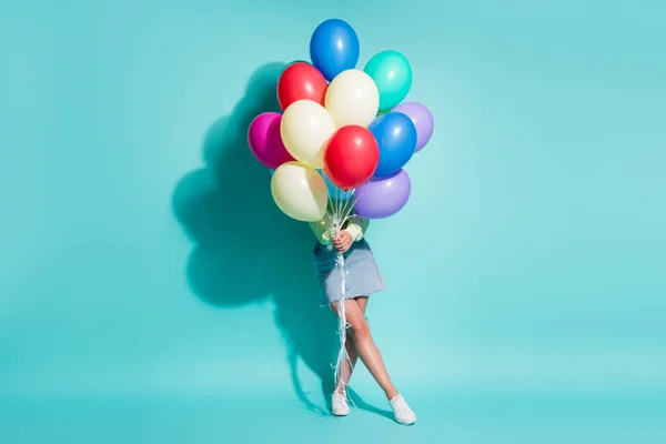 Foto de joven dama mantenga manojo globos cubrir a sí misma usar suéter verde mini jeans falda zapatillas aisladas de color azul fondo — Foto de Stock