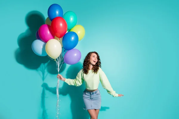 Фото милої молодої дівчини тримає багато кульок, дивлячись вгору порожній простір одягнути зелений светр коротка джинсова спідниця ізольований синій колір фону — стокове фото