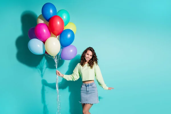 Foto van schattig jong meisje houden veel ballonnen dragen groene trui mini jeans rok geïsoleerde blauwe kleur achtergrond — Stockfoto