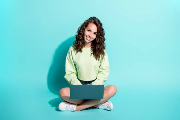 魅力的な若い女の子の写真は、床を保持するノートパソコンの笑みを浮かべて見てカメラを着用緑のセータースニーカー隔離された青の色の背景 — ストック写真