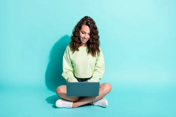 Foto de niña bastante joven sentarse piso mantenga netbook mirar pantalla escribiendo desgaste verde jersey aislado color azul fondo —  Fotos de Stock