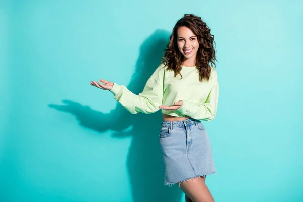 Foto retrato de encaracolado morena bonita mantendo as mãos para a frente mostrando no espaço vazio sorrindo isolado no fundo de cor teal brilhante — Fotografia de Stock