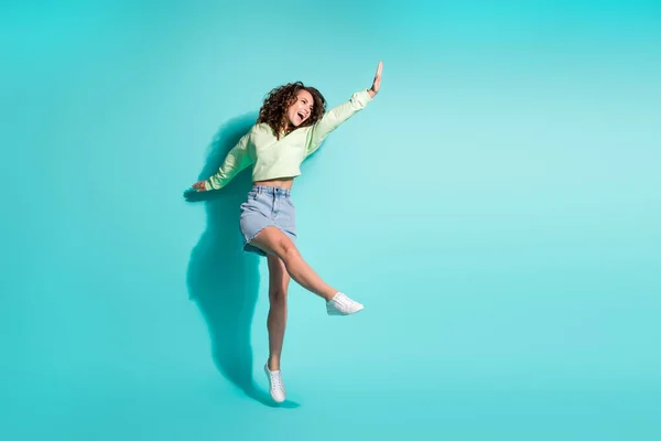 Foto de cuerpo entero tamaño de chica morena bailando saltando manteniendo la mano arriba cantando aislado sobre fondo de color verde azulado vibrante — Foto de Stock