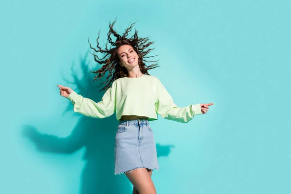 Retrato fotográfico de una joven alegre bailando sonriente con falda de mezclilla aislada sobre un vibrante fondo de color verde azulado —  Fotos de Stock