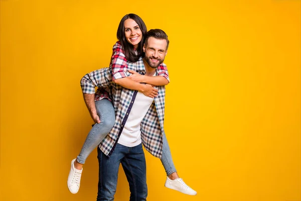 Foto portret van vrouw piggyback paardrijden echtgenoot geïsoleerd op levendige geel gekleurde achtergrond — Stockfoto