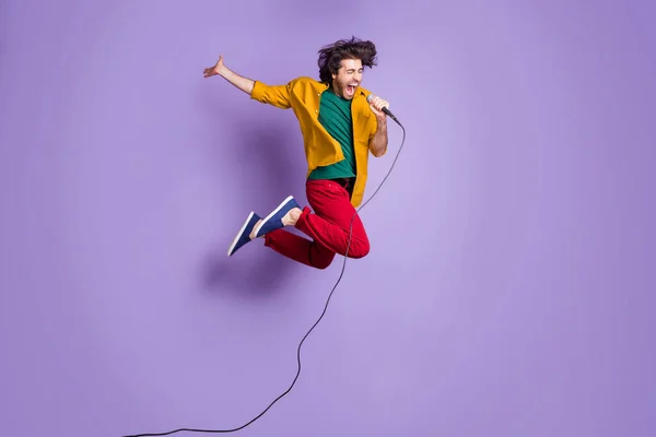 Ritratto fotografico a figura intera di pazzo che salta su cantando nel microfono isolato su uno sfondo di colore viola vivo — Foto Stock