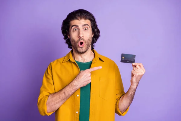 Bir elinde kredi kartı tutan şok olmuş bir adamın fotoğrafı canlı menekşe renkli arka planda izole edilmiş bir parmağı işaret ediyor. — Stok fotoğraf