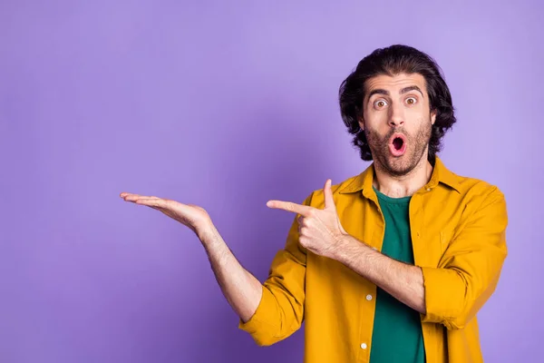 Фотопортрет здивованого чоловіка, який тримає порожній простір в руці вказуючи пальцем ізольований на яскраво-фіолетовому фоні — стокове фото