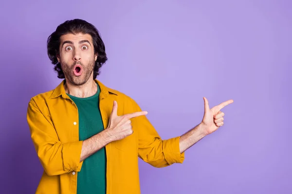 Фотопортрет здивованого чоловіка, який вказує два пальці на порожній простір ізольовано на яскраво-фіолетовому фоні — стокове фото