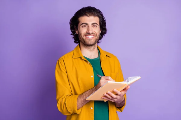 Photo of cheerful young stubble man happy positive smile write to-do list notebook isolated over purple color background