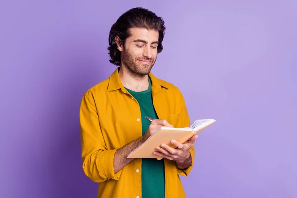Photo of young happy positive multiethnic man hold notebook make notes isolated over violet color background