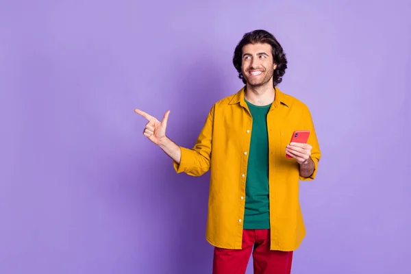 Foto av unga leende glad stilig man man man kille använda telefon peka finger titta i copyspace isolerad på violett färg bakgrund — Stockfoto