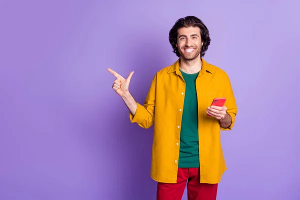 Foto av unga leende stilig man kille använder smartphone pekfinger i copyspace isolerad på violett färg bakgrund — Stockfoto