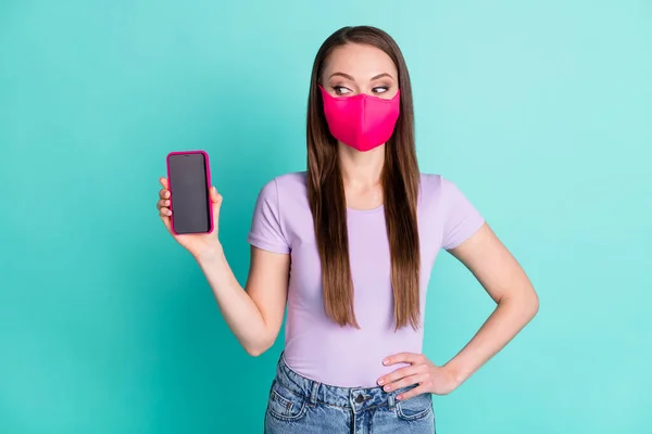 Foto retrato de menina olhando para tela sensível ao toque de smartphone com copyspace usando máscara de tecido isolado no fundo de cor teal brilhante — Fotografia de Stock