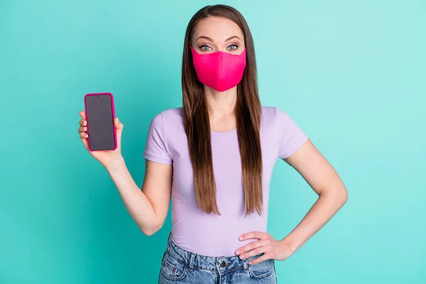 Foto retrato de menina brinco máscara de tecido mostrando touchscreen com copyspace isolado no fundo cor teal vívido — Fotografia de Stock