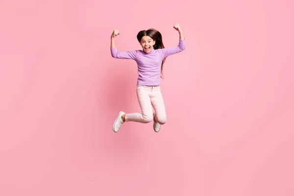 Full längd foto av galen liten flicka hoppa show triceps händer bära lila tröja byxor isolerade över rosa färg bakgrund — Stockfoto