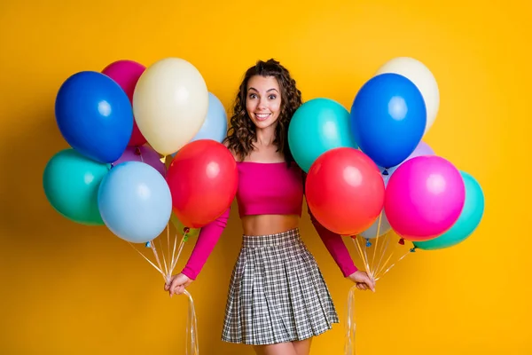 Foto ritratto di funky ragazza positiva che indossa prospettiva casuale con gonna a scacchi tenendo palloncini d'aria in entrambe le mani isolate su sfondo di colore giallo vivido — Foto Stock