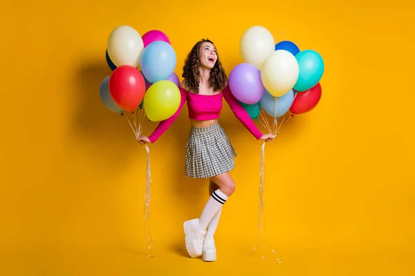 Foto de tamaño completo del cuerpo de la colegiala soñadora sosteniendo globos de aire sonriendo usando falda a cuadros calcetines largos recortados off-top aislados sobre fondo de color amarillo brillante — Foto de Stock