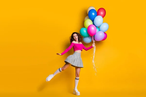 Foto de cuerpo entero de la muchacha bonita divertida que salta encima de los globos aéreos que sostienen altos sonriendo aislado en fondo amarillo brillante del color — Foto de Stock