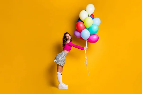 Foto de cuerpo de cuerpo entero de colegiala pequeña sosteniendo globos de colores sonriendo prepearing para la fiesta aislada sobre fondo de color amarillo brillante — Foto de Stock