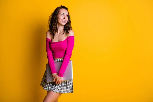 Photo of pretty charming lady hands hold closed laptop interested look up empty space smile wear pink top unclothed shoulders mini skirt isolated yellow color background