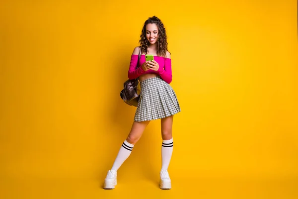Full length photo of cute lovely lady hold phone typing wear rucksack pink top uncoved ώμους mini skirt sneakers απομονωμένο κίτρινο χρώμα φόντο — Φωτογραφία Αρχείου