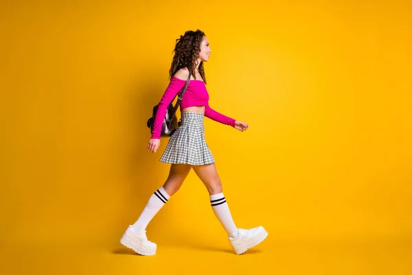 Full length profile photo of lovely lady wavy hairdo walk ακτινοβολούν χαμόγελο φορούν τσάντα ροζ top ακάλυπτους ώμους μίνι φούστα sneakers απομονωμένο κίτρινο χρώμα φόντο — Φωτογραφία Αρχείου