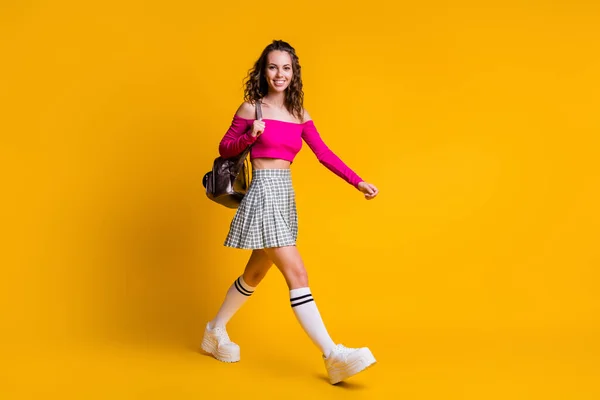 Full längd foto av ganska söt dam hålla ryggsäck promenad strålande leende bära rosa topp avtäckt axlar mini kjol strumpor sneakers isolerad gul färg bakgrund — Stockfoto