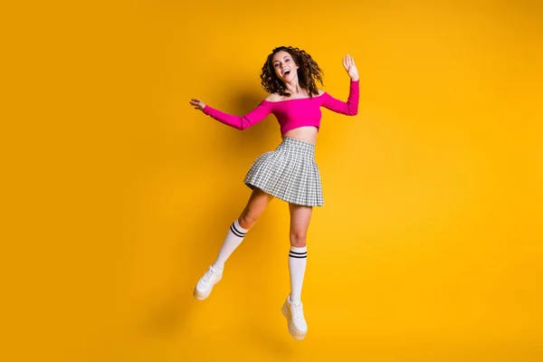 Foto retrato de menina saltando para cima alto vestindo rosa saia xadrez top meias longas tênis branco isolado no fundo colorido amarelo vívido — Fotografia de Stock