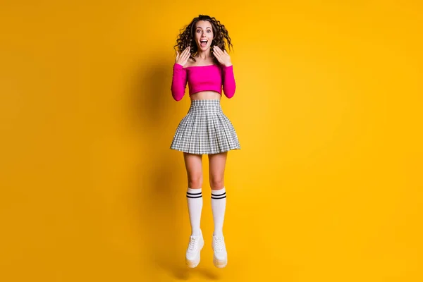 Foto retrato de niña saltando gritando manos cerca de la cara usando fucsia crop-top falda a cuadros calcetines hasta la rodilla zapatillas blancas aisladas sobre fondo de color amarillo brillante — Foto de Stock