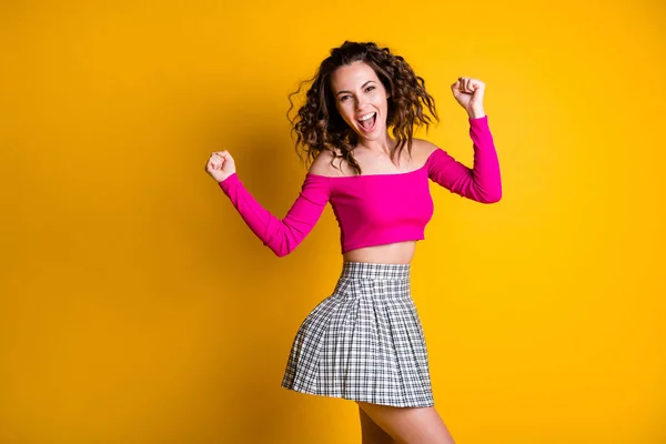 Foto retrato de animado jovem dançando segurando punhos para cima comemorando vestindo fuchsia saia quadriculada top isolado no fundo colorido amarelo vívido — Fotografia de Stock