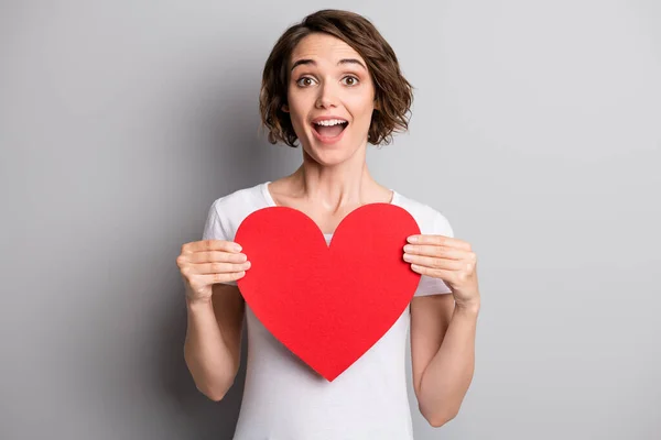 Foto av förvånad upphetsad ung kvinna hålla papper hjärta känslor hjärta romantisk gåva isolerad över grå färg bakgrund — Stockfoto