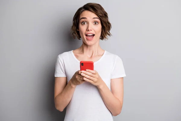 Foto de jovem menina bonita usar smartphone animado notícias surpresas informações isoladas sobre fundo de cor cinza — Fotografia de Stock
