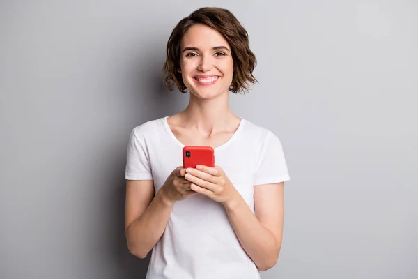 Foto de chica atractiva joven sonrisa feliz celebrar teléfono celular tipo de chat móvil aislado sobre fondo de color gris — Foto de Stock