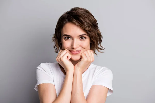 Foto de cabello castaño joven atractiva chica positiva disfrutar sonrisa manos tocar pómulos aislados sobre fondo de color gris —  Fotos de Stock