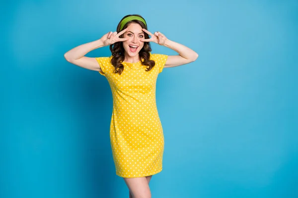 Foto van opgewonden meisje maken v-teken in de buurt gezicht dragen groen geel polka-stip rok geïsoleerd over blauwe kleur achtergrond — Stockfoto