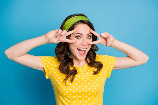 Портрет привлекательной возбужденной девушки сделать V-знак возле глаз носить горошек одежды изолированы на синем фоне цвета — стоковое фото