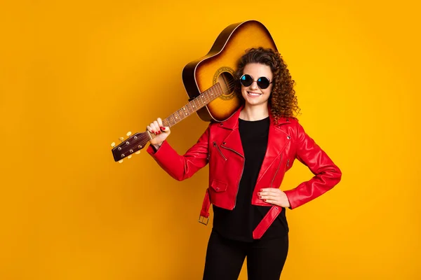 Portret van aantrekkelijke vrolijk golvend-harig meisje muzikant dragen gitaar geïsoleerd op fel gele kleur achtergrond — Stockfoto
