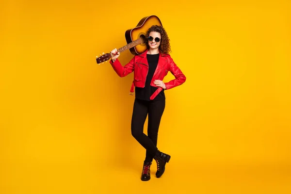 Full length body size view of attractive cheerful wavy-haired girl musician carrying bass guitar isolated on bright yellow color background