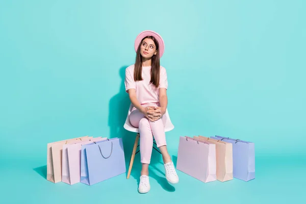 Foto de longitud completa de la silla sentada chica pensativa con bolsas de compras mirada espacio vacío pensar aislado sobre fondo de color verde azulado —  Fotos de Stock