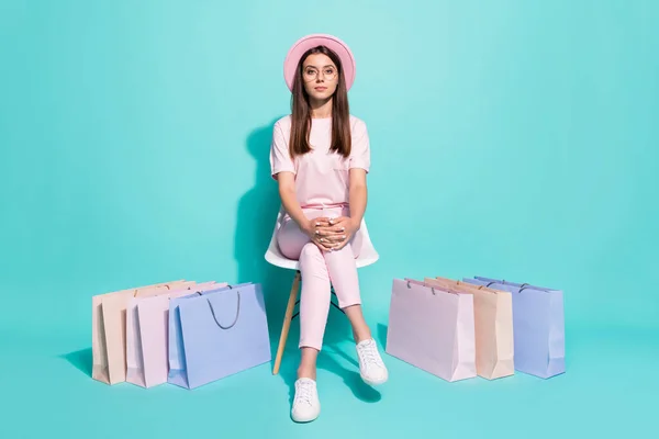 원문 기사보기 진지 한 여학생 이 의자에 앉아 쇼핑백을 두르고 청록색 배경에 핑크 색 선 모자를 쓰고 있는 사진 — 스톡 사진