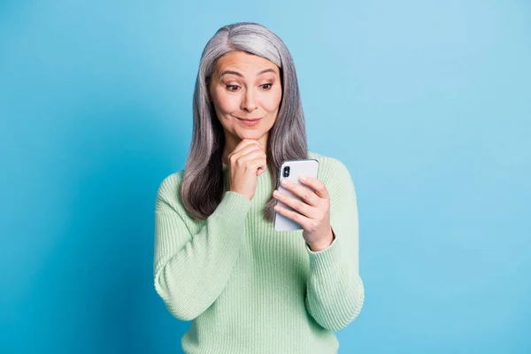 Фото удивленной пожилой женщины взгляд в сотовый телефон сенсорный подбородок одет зеленый пуловер изолированы на синем фоне цвета — стоковое фото