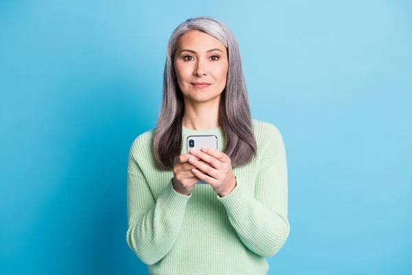 Портрет улыбающейся пожилой женщины держать телефон одет зеленый свитер изолирован на синем фоне цвета — стоковое фото