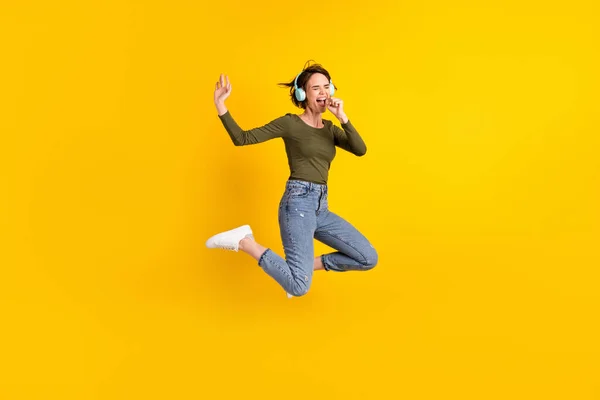 Foto de longitud completa de chica loca salto cantar canción uso de la mano como micrófono desgaste auriculares inalámbricos aislados sobre fondo de color amarillo brillante —  Fotos de Stock